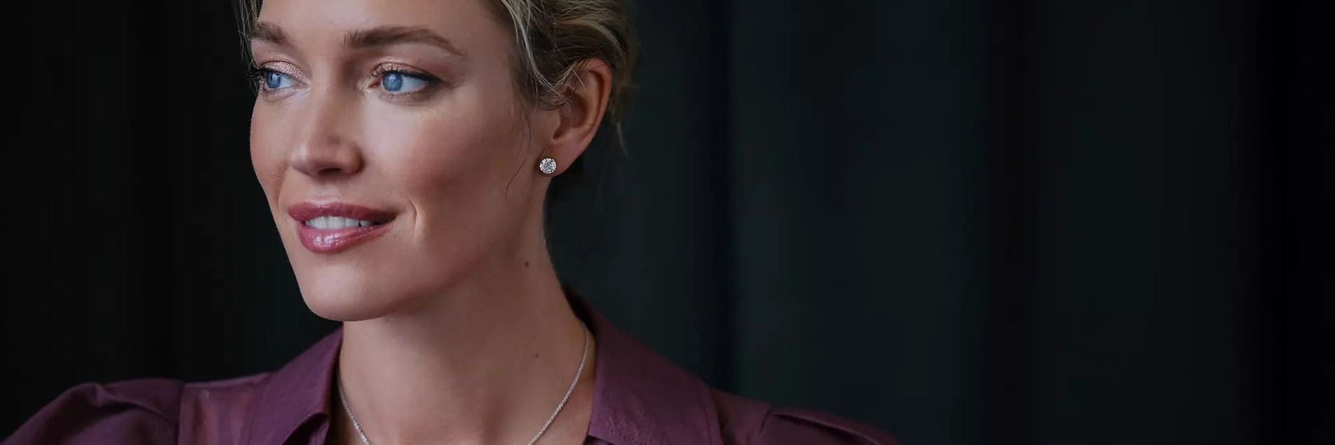 Woman wearing maroon blouse, diamond stud earrings and diamond pendant necklace