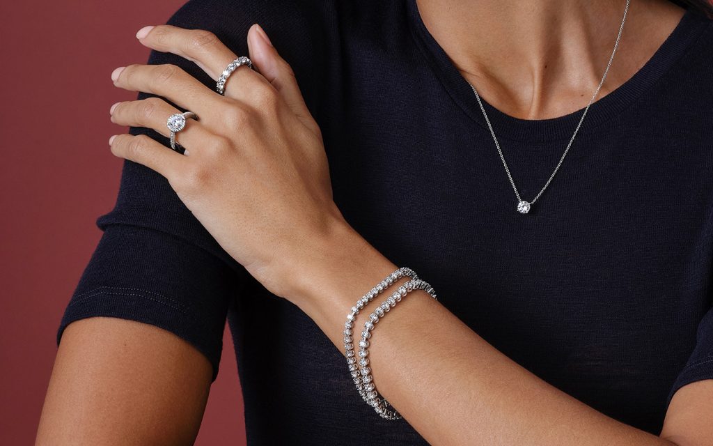 Close up of woman’s hand on her shoulder, she is wearing diamond jewelry.