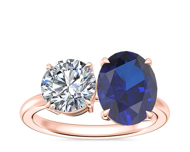 Crafted from luxurious 18k rose gold, this engagement ring features stunning two-stone design. An oval-cut sapphire adds beautiful brilliance next to a round, princess, pear, asscher, emerald-cut, radiant, cushion, marquise, heart, or oval-cut stone.