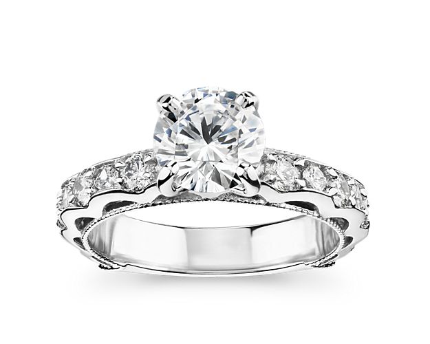 This magnificent platinum engagement ring boasts scalloped detailing along the shank, accented by a row of prong-set diamonds and vintage-inspired milgrain trim. This setting is custom made to fit your beautiful center stone.