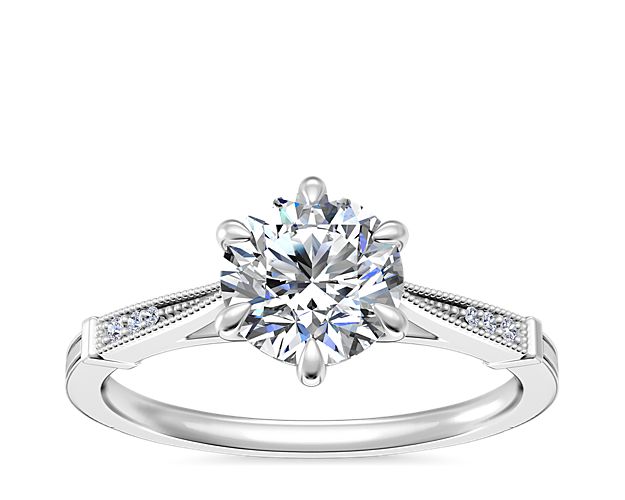 This stunning platinum engagement ring features a classic six-prong design that gracefully holds the center stone aloft. Intricate milgrain detail along the sides and sparkling accent diamonds complete the effect with a touch of vintage-inspired nostalgia.