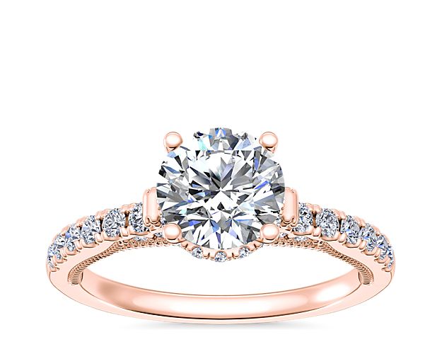 Celebrate your love with this stunning engagement ring featuring a diamond gorgeously accented by a hidden halo and pave-set diamond detail along the shank. Crafted in lustrous 14k rose gold, it features delicate lace-inspired detail along the profile, with scroll designs accenting the shoulder.