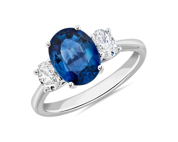 Simple and stunning, this ring features a vividly blue oval-cut sapphire nestled between two stunning oval-cut diamonds. It is crafted from 14k white gold that promises lasting luxury and a bright gleam.