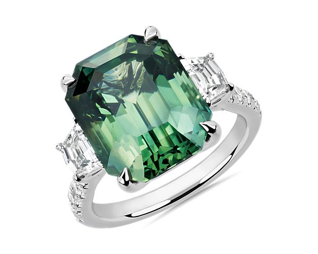 This stunning ring features an incredible radiant cut green sapphire.  Trapezoid diamond side stones flank the side of the sapphire while sparkling brilliant cut diamonds cascade down along the band of this 18k white gold creation.  This ring is accompanied by gemstone report #:CDC22081154.