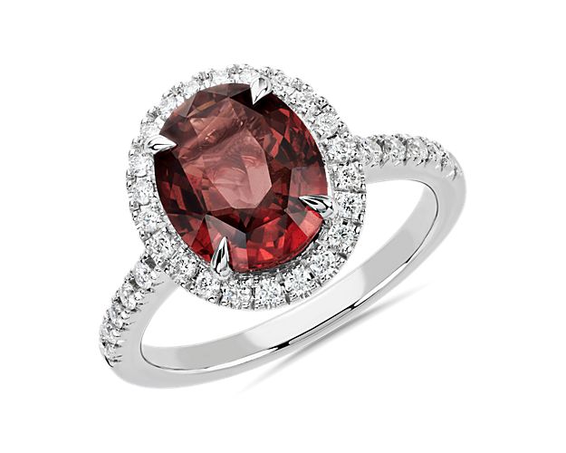 This ring features an oval shaped dark orange sapphire with a slightly reddish hue.  Set in 18k white gold, this ring is also set with shimmering diamonds that create a beautiful halo as well as a diamond studded band.  This ring is accompanied by gemstone report #:CDC22081158.