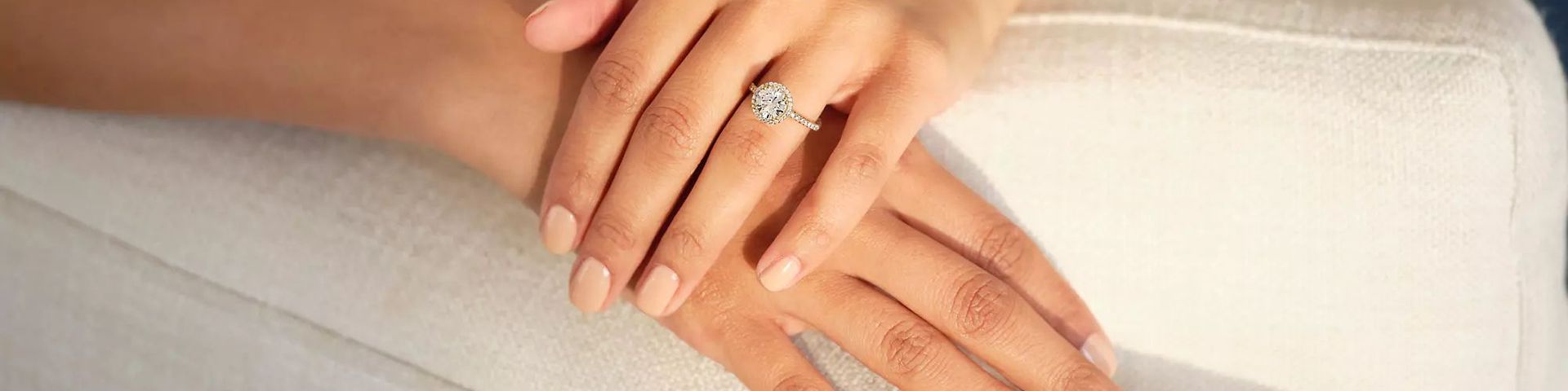 crossed hands of woman wearing a lab-grown engagement ring resting on sofa arm