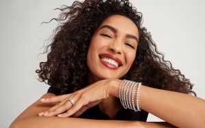 Smiling woman wearing multiple gold tennis bracelets of varying carat weights.